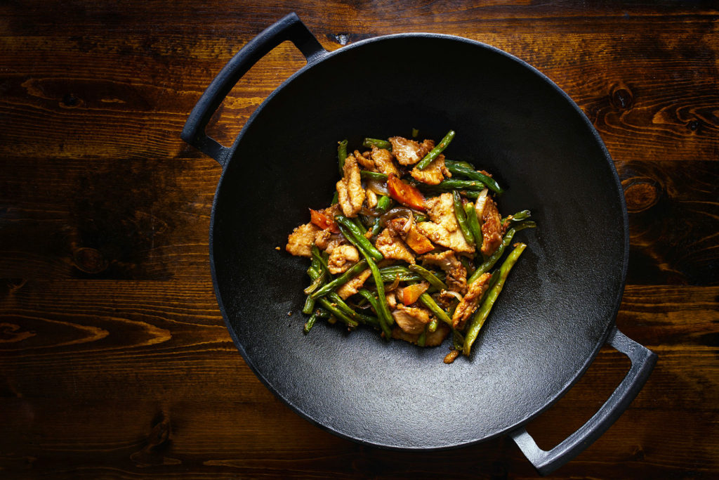 Cast iron wok with stir fry vegetables and chicken seasoned on a wood counter