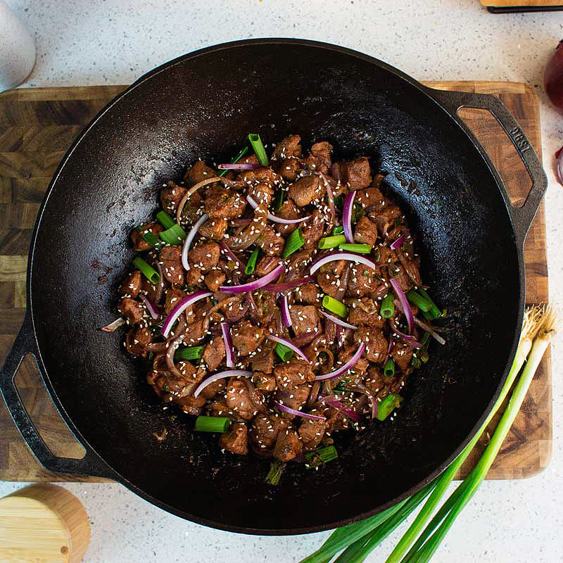 Lodge Pro Cast Iron Wok with stir fry duck covered in sesame seeds on a wood cutting board