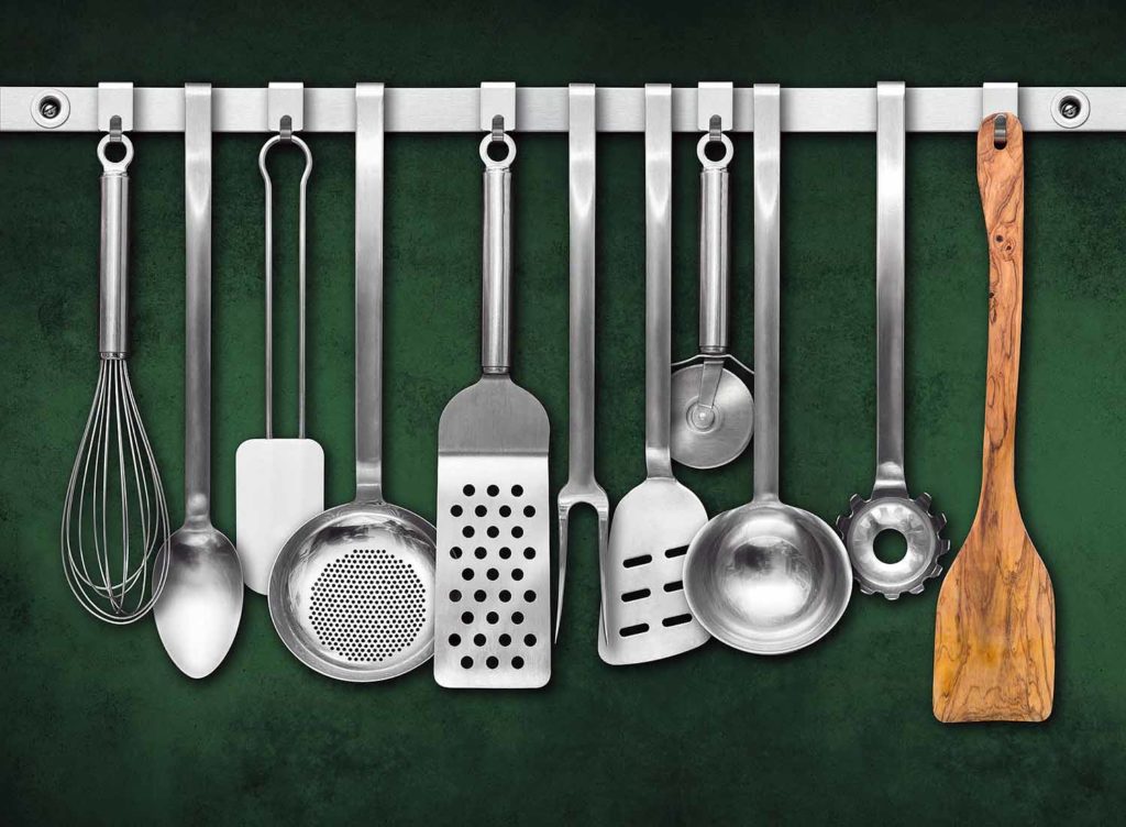 Stainless steel kitchen utensils hanging from hooks, and one wooden spatula on the right.