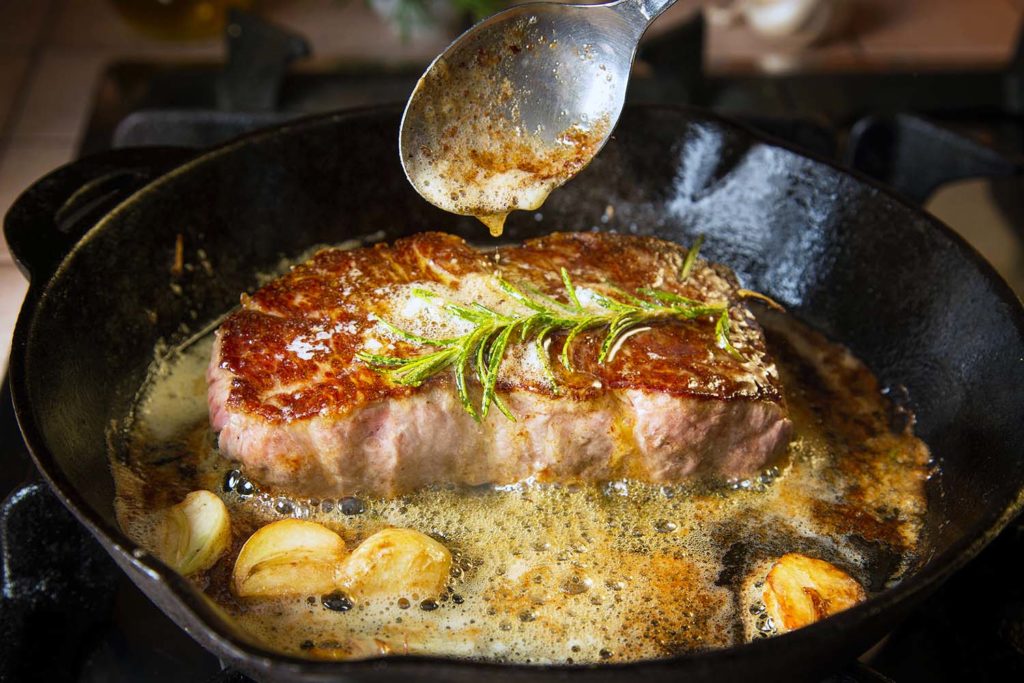 Basting flat iron steak with butter in a cast iron pan with garlic and rosemary