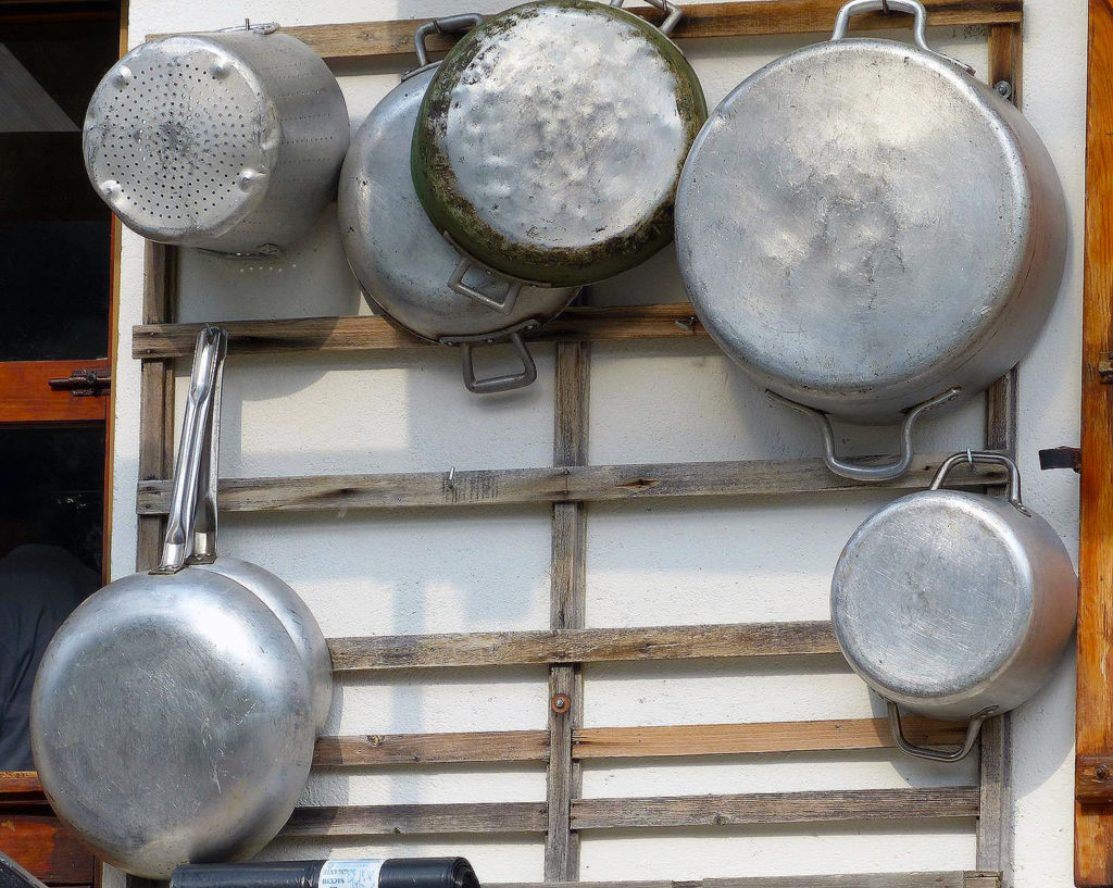 Banged up aluminum pots hanging on a wooden rack