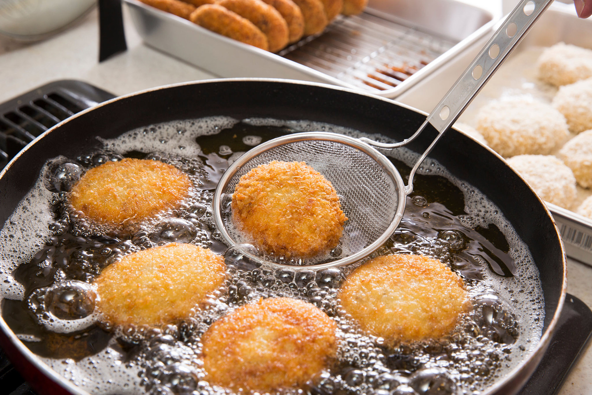 Best Deep Frying Utensils used in a pot of hot oil and croiquets, dishes and ingredients in the background