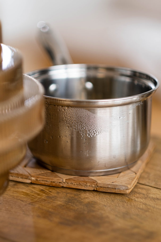 small stainless steel pot on wood pad on counter condensation on sides of pot